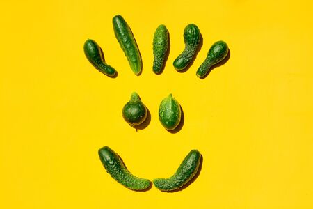 Different sizes and forms cucumbers on a yellow background forms a smiling face. Smile, face, emoji, smiley, happy smiley, happy emoji, smiling emoji. Top view. Concept for designers with copy space.の写真素材