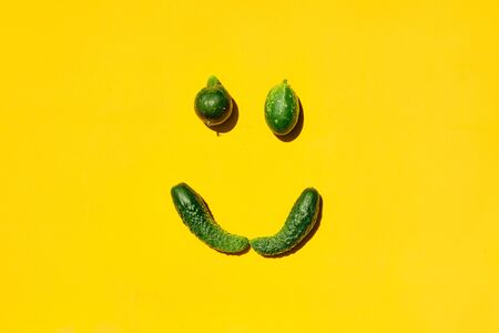 Different sizes and forms cucumbers on a yellow background forms a smiling face. Smile, face, emoji, smiley, happy smiley, happy emoji, smiling emoji. Top view. Concept for designers with copy space.の写真素材