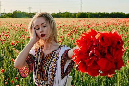 Long-haired blonde young woman in a white short dress on a field of green wheat and wild poppies. Slim sexy girl. A concept of freedom and freshness. Summer vacation female symbol. Summertime flowers.の写真素材