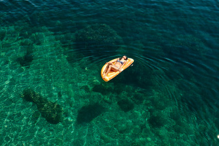Slim young woman in bikini and sunglasses on the air mattress floats in the open sea. Enjoying...