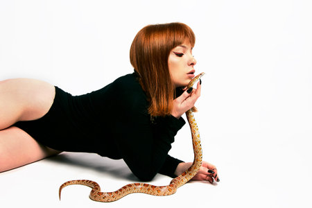Beautiful woman in black bodywear and snake. Ginger model girl with fashion perfect make up.