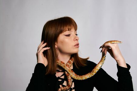 Beautiful woman in black bodywear and snake. Ginger model girl with fashion perfect make up. High end retouch. White background. Young woman with perfect fresh skin. Woman with snake around her.の写真素材
