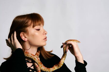 Beautiful woman in black bodywear and snake. Ginger model girl with fashion perfect make up. High end retouch. White background. Young woman with perfect fresh skin. Woman with snake around her.の写真素材