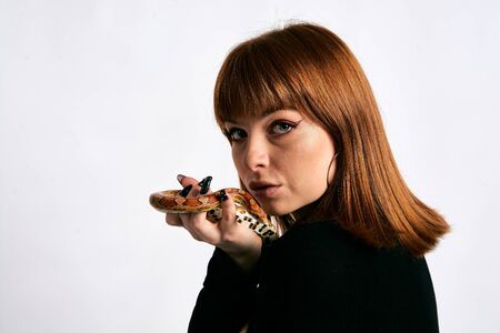 Beautiful woman in black bodywear and snake. Ginger model girl with fashion perfect make up. High end retouch. White background. Young woman with perfect fresh skin. Woman with snake around her.の写真素材