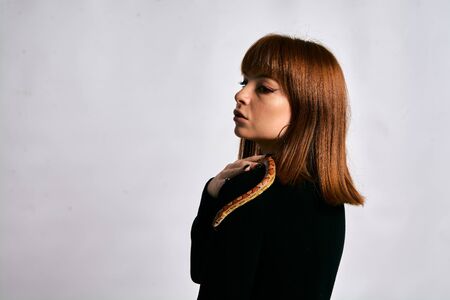 Beautiful woman in black bodywear and snake. Ginger model girl with fashion perfect make up. High end retouch. White background. Young woman with perfect fresh skin. Woman with snake around her.の写真素材