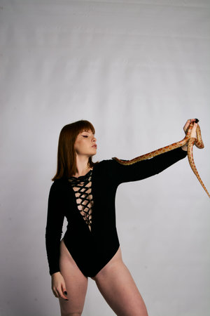 Beautiful woman in black bodywear and snake. Ginger model girl with fashion perfect make up. High...