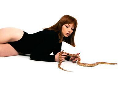 Beautiful woman in black bodywear and snake. Ginger model girl with fashion perfect make up. High end retouch. White background. Young woman with perfect fresh skin. Woman with snake around her.の写真素材