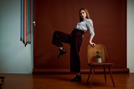 Mininalism style classic studio photo set of the young independent woman. Gorgeous young female in classic suit, black shoes and grey coat. Vintage chair. Woman's clothes. Fashionable clothes.の写真素材