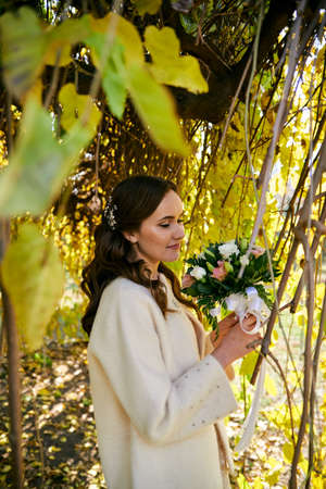 Warm autumn portrait of young pretty woman dressed in white jacket with flower bouquet in her hand.の写真素材