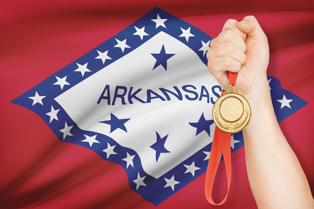 Sportsman holding gold medal with State of Arkansas flag on background. Part of a series.の写真素材