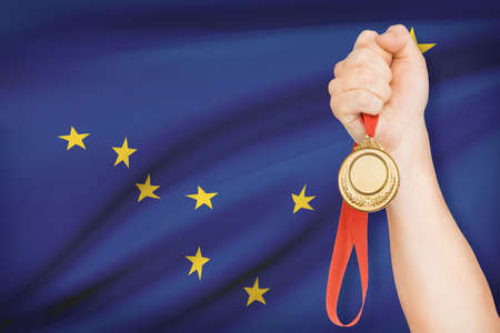 Sportsman holding gold medal with State of Alaska flag on background. Part of a series.の写真素材