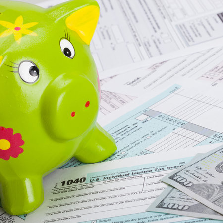 Hundred USA dollars banknote and piggy bank over US tax form