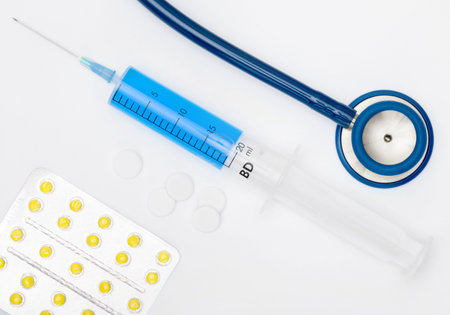 Stethoscope, pills and a syringe with blue liquid inside on grey backgroundの写真素材