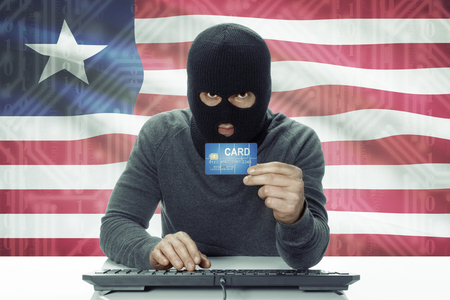 Dark-skinned hacker with credit card and flag on background - Liberiaの写真素材