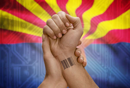 Barcode ID number tattoo on wrist of dark skinned person and USA states flag on background - Arizonaの写真素材