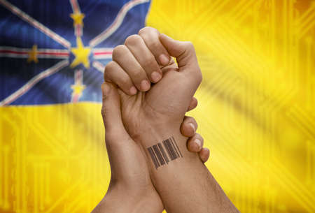 Barcode ID number tattoo on wrist of dark skinned person and national flag on background - Niueの写真素材