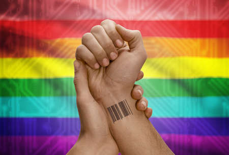Barcode ID number tattoo on wrist of dark skinned person and national flag on background - LGBT people flagの写真素材