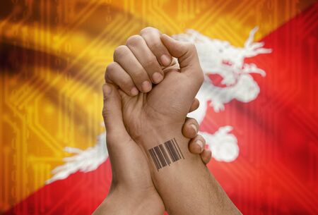 Barcode ID number tattoo on wrist of dark skinned person and national flag on background - Bhutanの写真素材