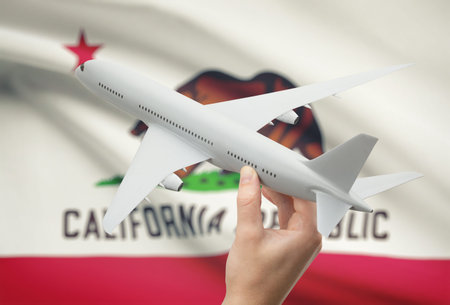 Airplane in hand with local US state flag on background - California