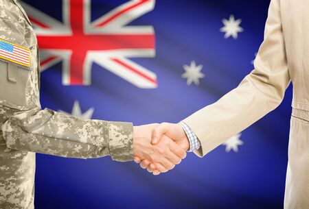 American soldier in uniform and civil man in suit shaking hands with national flag on background - Australiaの写真素材