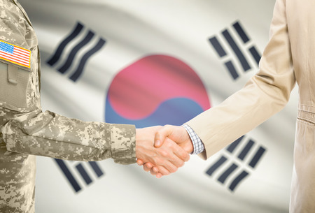 American soldier in uniform and civil man in suit shaking hands with national flag on background - South Koreaの写真素材
