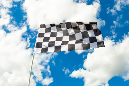 Checkered flag on flagpole waving in the wind with clouds on backgroundの写真素材