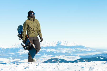 Snowboarder holding his board in hand and taking a walk at the top of a mountainの写真素材