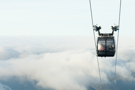 Cable car cabin going up above the clouds to the top of a mountain at a ski resort areaの写真素材