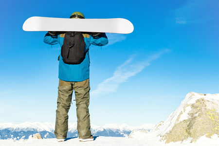 Winter sports concept - young male snowboarder holding his snowboard on his shoulders at the very top of a mountain and enjoying the scenery - outdoors shotの写真素材