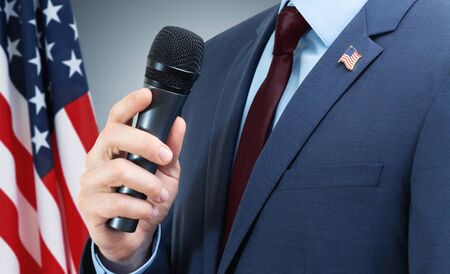White man in suit holding microphone in hand with USA flag on backgroundの写真素材