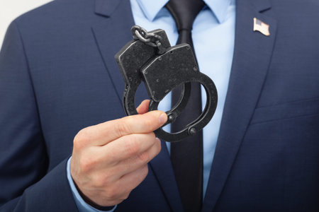 Man in suit holding handcuffs in hand with USA flag pin on his chest