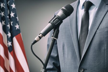 Man in suit standing next to microphone with USA flag on backgroundの写真素材