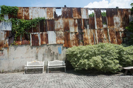 Old rusty iron fence and bench in the courtyard of the house.の写真素材