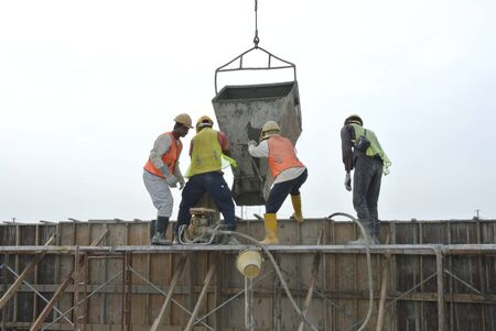 : A group of construction workers pouring concrete using concrete bucket into the timber formwork.のeditorial素材