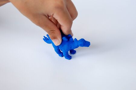 Children hand holding a blue dinosaur model. The model was made from rubber isolated on white background.の写真素材