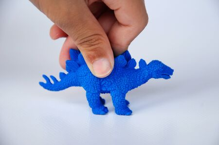 Children hand holding a blue dinosaur model. The model was made from rubber isolated on white background.の写真素材