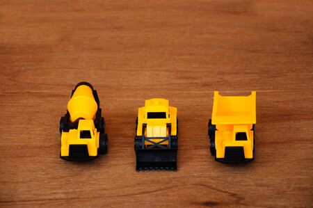 Group of small heavy construction machine toy, lorry, bulldozer and concrete mixer. All made of plastic isolated on a wood grain texture background.の写真素材