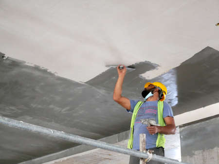 KUALA LUMPUR, MALAYSIA -APRIL 16, 2020: Construction site workers are doing ceiling soffit skim coat work at the construction site. Two layers base and final coat apply to get the smooth surface.のeditorial素材