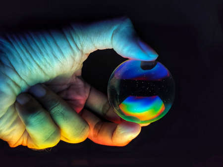 A hand holding a colourful effect lighting crystal ball with three fingers isolated on black background.の写真素材