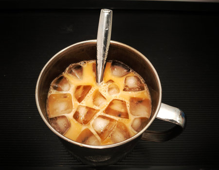 Close up of 'Tea Tarik' with ice cube in the steel mug isolated on black background.