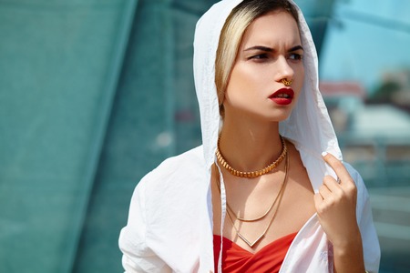 Portrait of a young girl in a white windbreaker against the background of a glass wall. Red lips and decorations.の写真素材