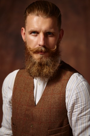 Close portrait of a man with a beard and mustache. Brown jacket, white shirt, brown background.の写真素材
