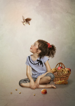  Little girl looking at the bird, basket with grapes next to a girlの写真素材