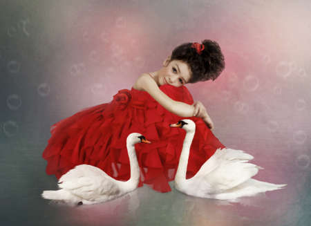 Little girl in a beautiful red dress surrounded by white swansの写真素材