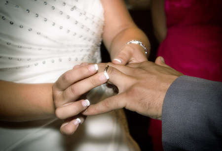 Close up hands of bride and groom putting on a wedding ringsの写真素材