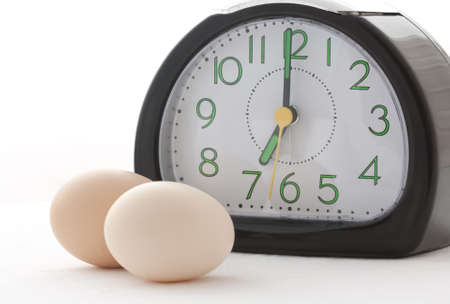 Two eggs along with clock showing time 7AM, a breakfast time on isolated white background.の写真素材