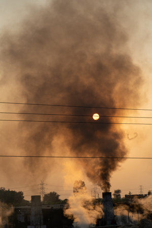 Pollution smoke out of jaggery making factory in India, against sun in the sky.の写真素材