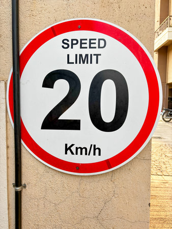 Closeup of a speed limit sign board displayed on a cream colour wall, the board show 20km/h speed...