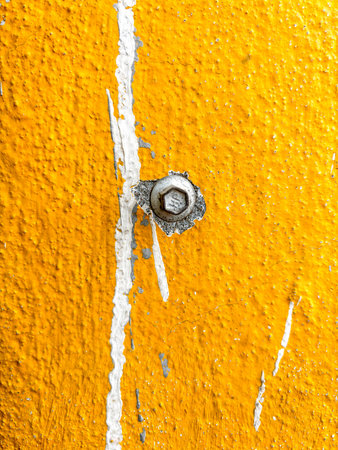 A yellow wall with a white line and a small hole in it. The hole is covered with a bolt