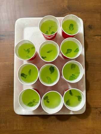 A tray of green drinks with mint leaves in them. The drinks are in cups and are arranged in a grid...